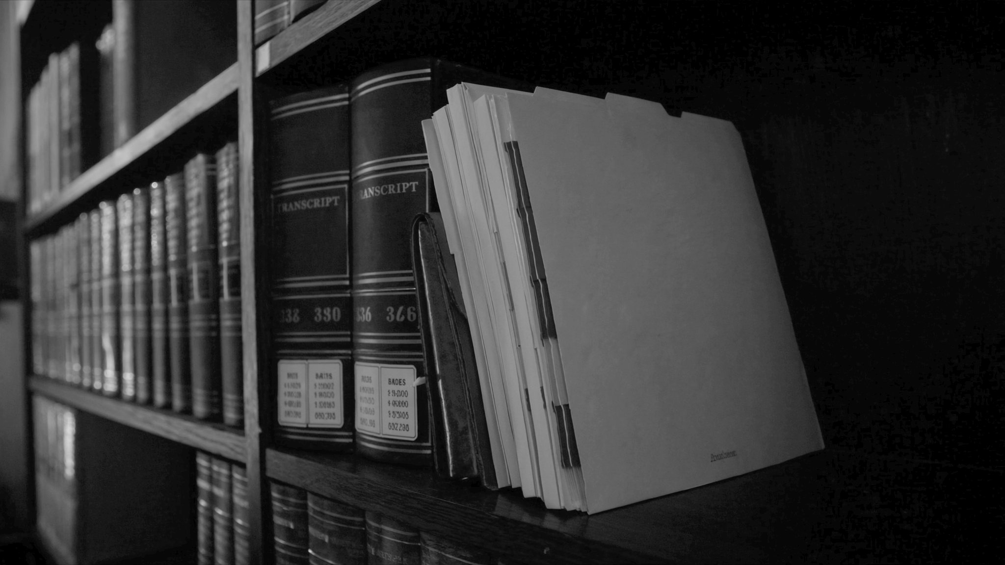 Bound volumes lettered Transcript on a dark shelf beside a file folder bristling with coloured index tabs.